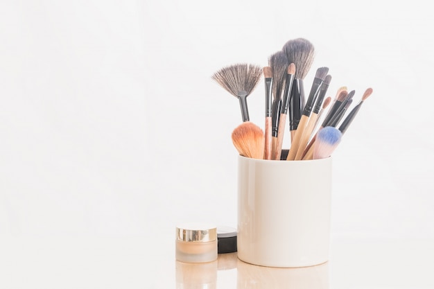 brosses de maquillage en titulaire et cosmétiques isolées sur blanc