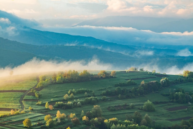 Brouillard blanc sur les montagnes depuis la campagne, lumière du coucher du soleil. Paysage de montagnes dans le brouillard.