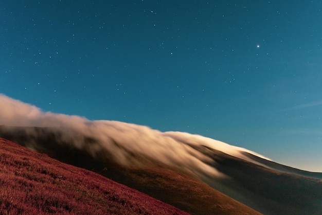 Brouillard épais moelleux couvrant le sommet de la montagne avec une forêt de conifères verte sous un ciel bleu dans une nuit lumineuse en vue du soir d'automne