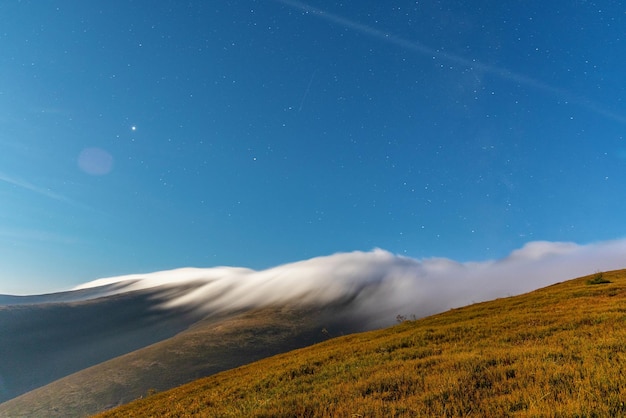 Brouillard épais moelleux couvrant le sommet de la montagne avec une forêt de conifères verte sous un ciel bleu à la nuit claire en vue du soir d'automne