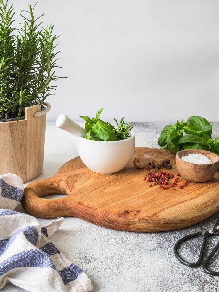 Brousse de romarin frais dans des pots en bois, brindilles de basilic vert frais, mortier blanc avec un pilon, sel et ail sur un plateau rond en bois Vue de dessus.
