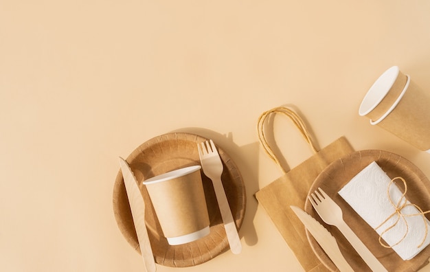 Brown craft sac jetable et vaisselle tasse, assiette et fourchette en bois, couteau sur une surface brune vue de dessus à plat