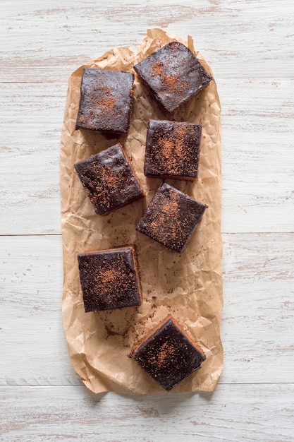 Brownie classique fraîchement cuit sur parchemin sont disposés sur une surface en bois blanc