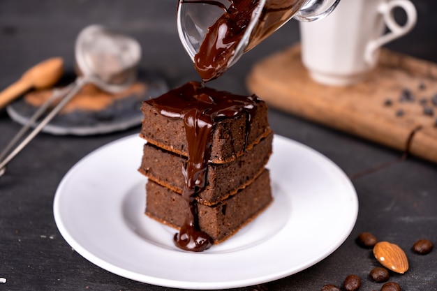 Brownies au cacao versant avec du chocolat noir fondu sur une plaque blanche.