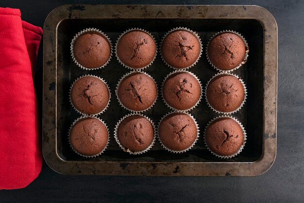Brownies au chocolat muffins sur plaque à pâtisserie et maniques rouges sur fond noir Cupcake maison juste cuit