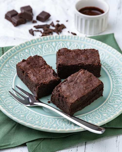 Brownies sur une plaque verte avec des morceaux de chocolat et du sirop sur une table en bois blanc