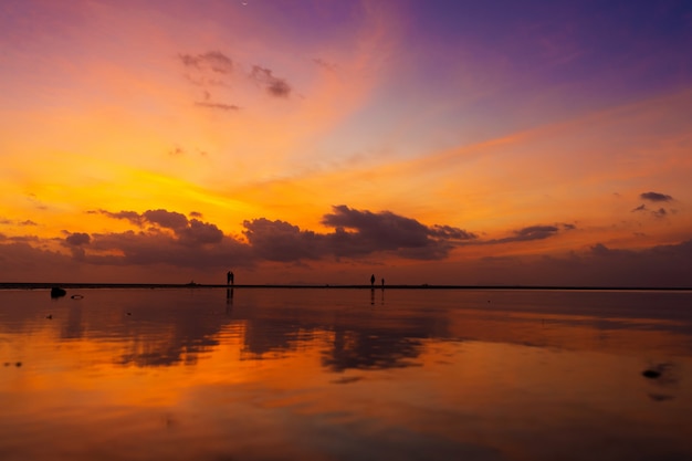 Brûler un ciel lumineux pendant le coucher du soleil sur une plage tropicale. Coucher de soleil pendant l'exode, la force des gens qui marchent sur l'eau