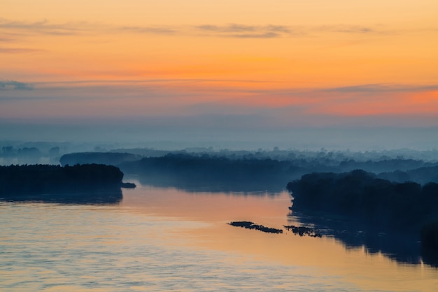 Brume mystique du matin au-dessus de la large vallée de la rivière. Lueur d'or de l'aube dans le ciel.