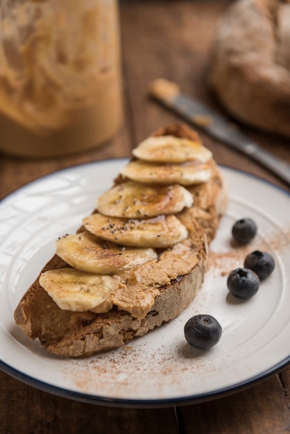 Brunch végétalien avec pain rustique grillé, beurre d'arachide, banane, bleuets, cannelle, graines de chia et sirop d'érable.