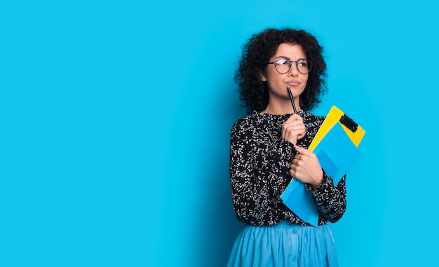 brune aux cheveux bouclés tient un stylo et des livres