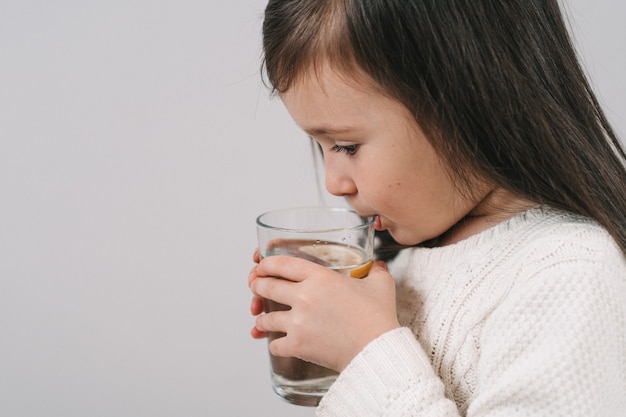 La brune boit de l'eau dans un verre transparent. La jeune fille tient un verre d'eau.