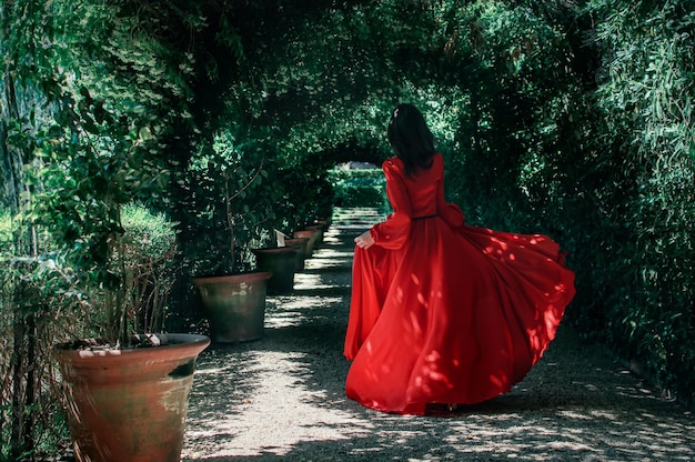 Une brune brûlante en robe rouge se promène dans les jardins