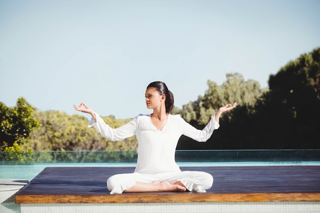 Brune calme faisant du yoga au bord de la piscine