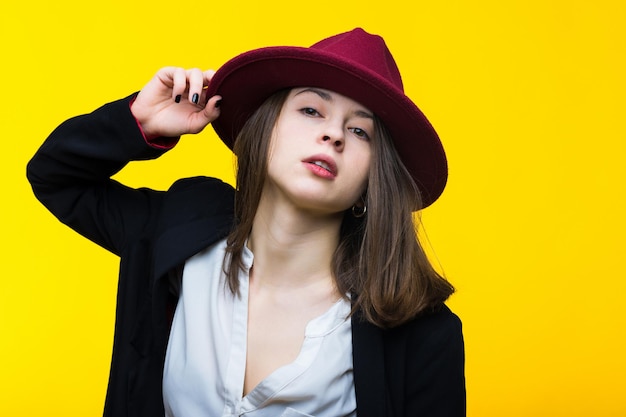 Brune en costume noir, chemise blanche et chapeau sur fond jaunePortrait émotionnel en studio