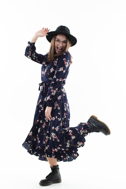 Une brune dans une longue robe à fleurs avec un chapeau pose pour la caméra dans le studio. Portrait émotionnel