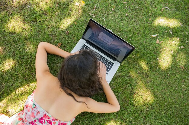 Brune élégante couchée sur l&#39;herbe en utilisant son ordinateur portable