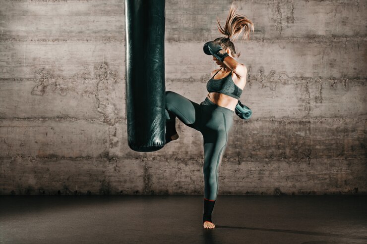 Une brune forte et dévouée avec une queue de cheval, en tenue de sport, pieds nus et avec des gants de boxe dans un sac de sport.