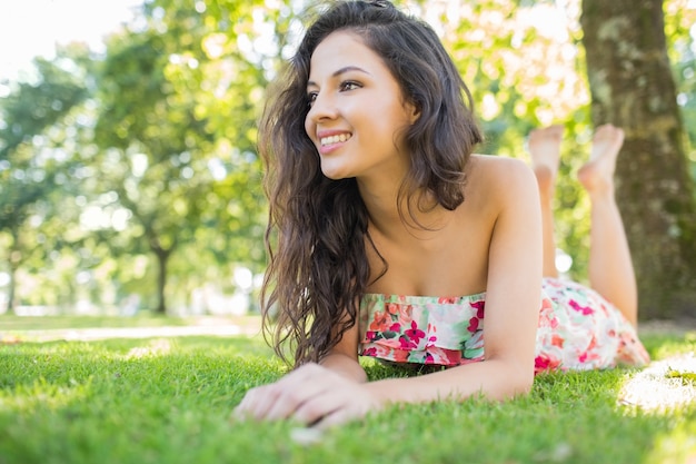 Brune joyeuse élégant allongé sur une pelouse en détournant les yeux