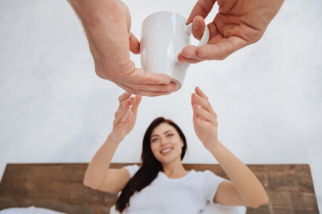 Brune Millénaire Assise Sur Un Lit Avec Ses Bras Tendus Tout En Recevant Une Tasse De Café D'un Homme Le Matin