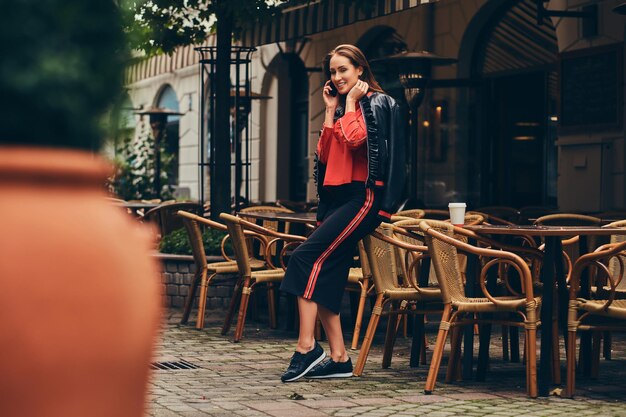 Une brune à la mode vêtue d'un vêtement élégant s'amuse près du café