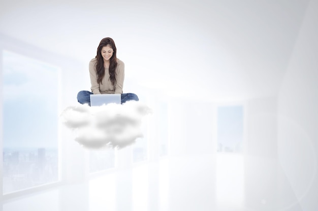 Brunette assise sur un nuage à l'aide d'un ordinateur portable contre un hall blanc brillant avec des colonnes