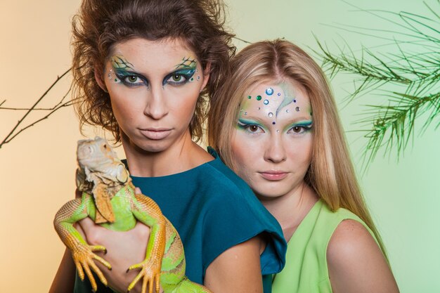 Brunette et blonde avec un iguane prédateur dans leurs mains. Image d'une femme prédatrice et d'une fille douce avec un animal en captivité