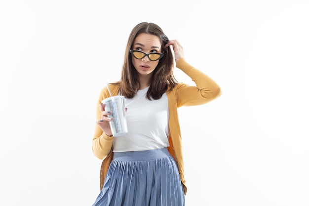 Brunette dans un pull jaune boit du café dans un grand verre brillant