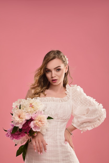 Brunette dans une robe d'été sur une rose avec un bouquet de fleurs dans ses mains.