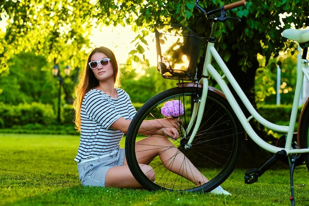 Brunette est assise sur la pelouse verte à vélo et tient un bouquet de fleurs dans le parc.