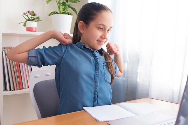 Brunette étudie à l'ordinateur à la maison en faisant ses devoirs en communiquant sur le réseau en étirant les bras