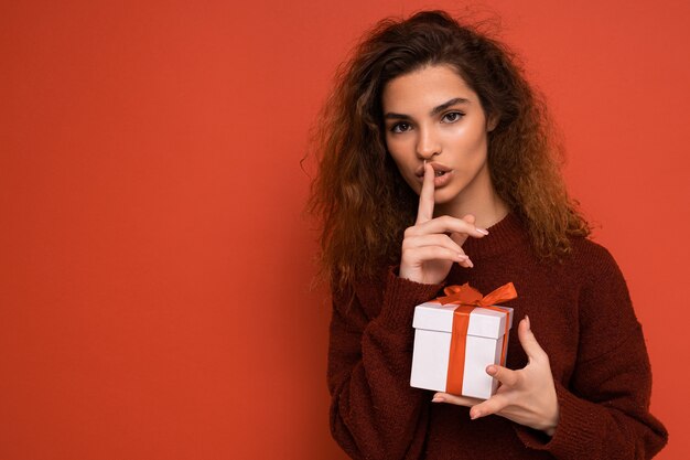 Brunette femme bouclée isolée sur fond rouge mur portant un pull rouge