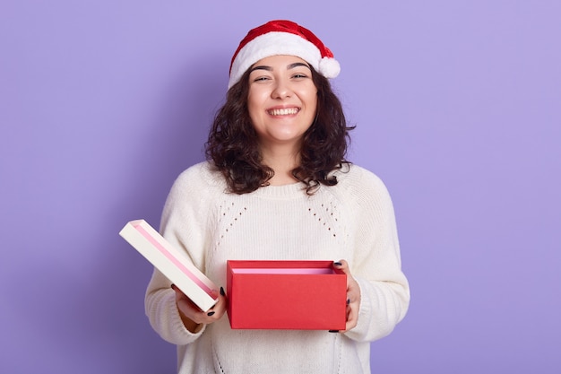 Brunette femme souriante en bonnet de Noel avec boîte-cadeau ouverte