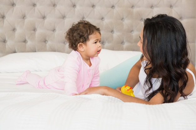 Brunette joue avec son bébé et un canard sur le lit