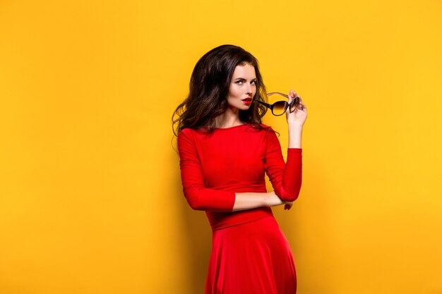 Brunette en lunettes de soleil et robe rouge posant