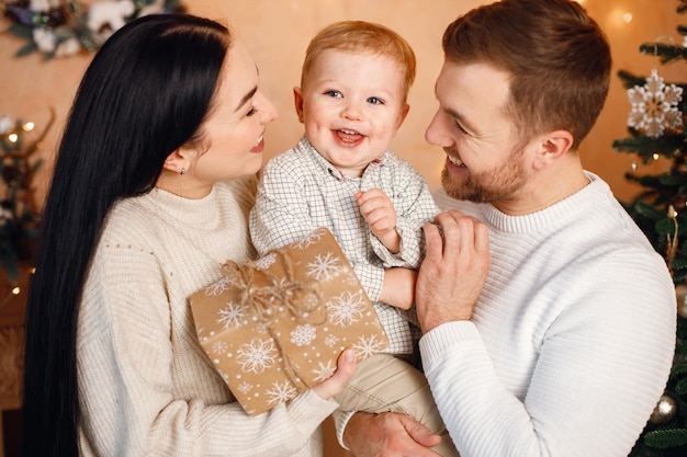 Brunette mère père et petit fils debout près de l'arbre de Noël et étreignant