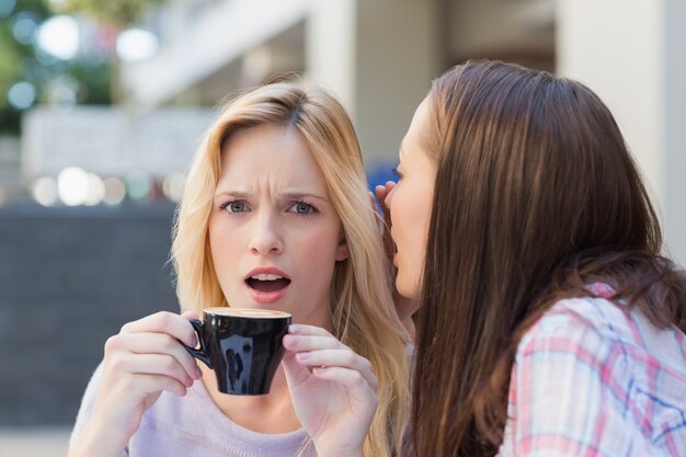 Brunette révélant un secret à son amie en buvant un café