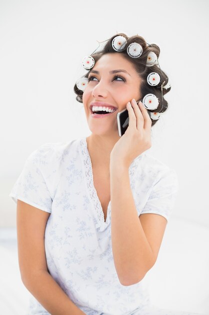 Brunette en riant dans les rouleaux de cheveux sur le téléphone sur le lit