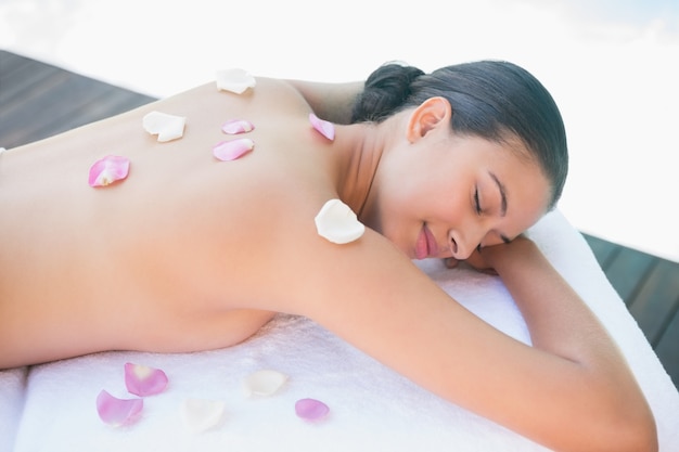 Brunette souriante allongée sur une serviette avec des pétales de rose