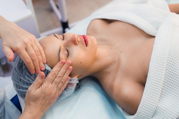 Brunette souriante bénéficiant d'un massage de la tête dans le spa de santé