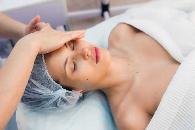 Brunette souriante bénéficiant d'un massage de la tête dans le spa de santé