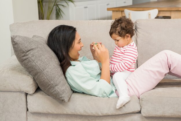 Brunette souriante jouant avec son bébé sur le canapé