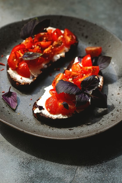 Bruschett aux tomates cerises fromage cottage basilic herbes ail poêlé sur fond gris lumière dure naturelle