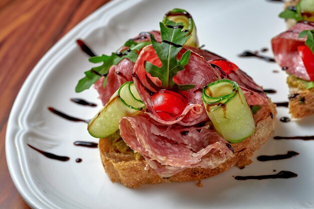 Bruschetta au salami et tomates dans une assiette blanche sur un fond en bois