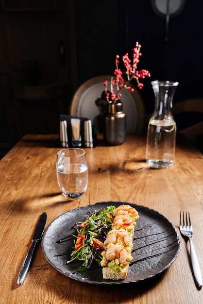 bruschetta aux crevettes et salade sur une assiette sombre sur une table en bois dans un bel intérieur vertical