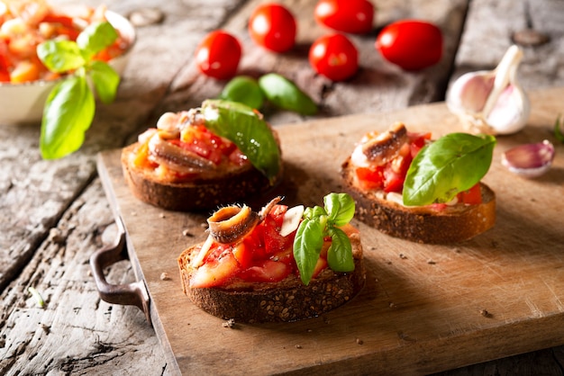 Photo bruschetta aux tomates, anchois au basilic et huile d'olive sur planche de bois. apéritif ou collation italienne traditionnelle, antipasti