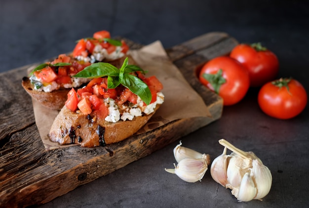 Bruschetta aux tomates, basilic et fromage du village sur planche de bois avec table de tomates. Apéritif ou collation italienne traditionnelle