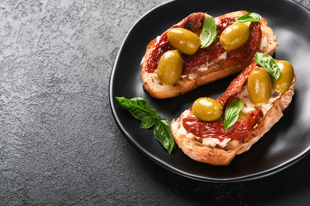 Bruschetta aux tomates séchées au soleil Toast ou sandwich à la ricotta tomates séchées au soleil et herbes de Provence au basilic servi sur plaque noire sur fond noir table Mise au point sélective