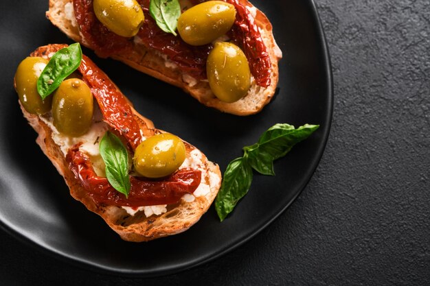 Bruschetta aux tomates séchées au soleil Toast ou sandwich à la ricotta tomates séchées au soleil et herbes de Provence au basilic servi sur plaque noire sur fond noir table Mise au point sélective