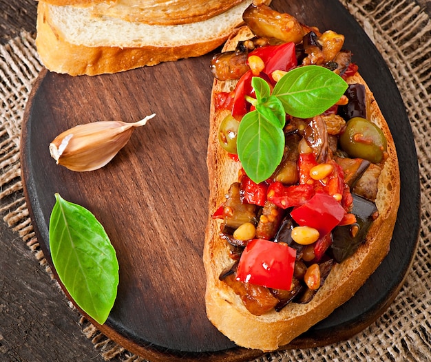 Bruschetta caponata aux raisins secs et pignons de pin décorée d'une feuille de basilic