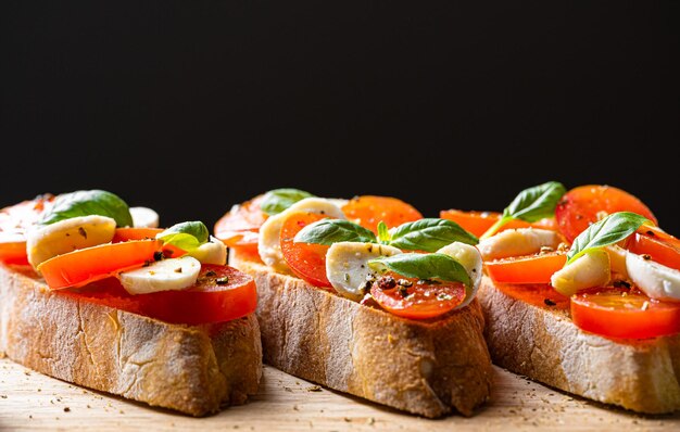 Photo bruschetta caprese feuilles de basilic frais tomates aromatiques mûres et mozzarella italienne sur bruschetta arrosée d'huile d'olive et saupoudrée de poivre et d'herbes